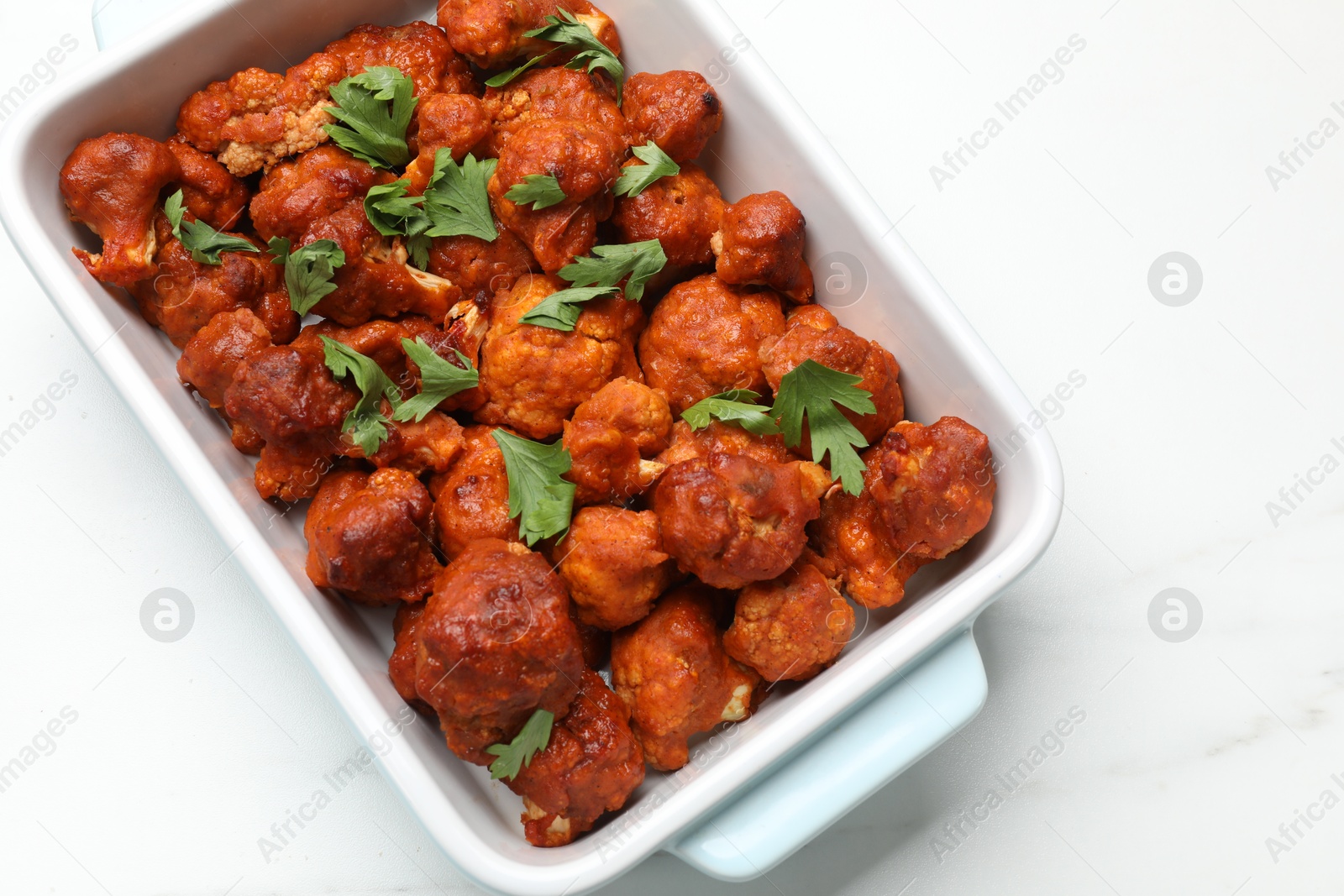 Photo of Baked cauliflower buffalo wings with parsley in baking dish on white marble table, top view