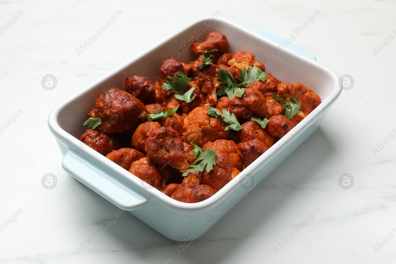 Photo of Baked cauliflower buffalo wings with parsley in baking dish on white marble table