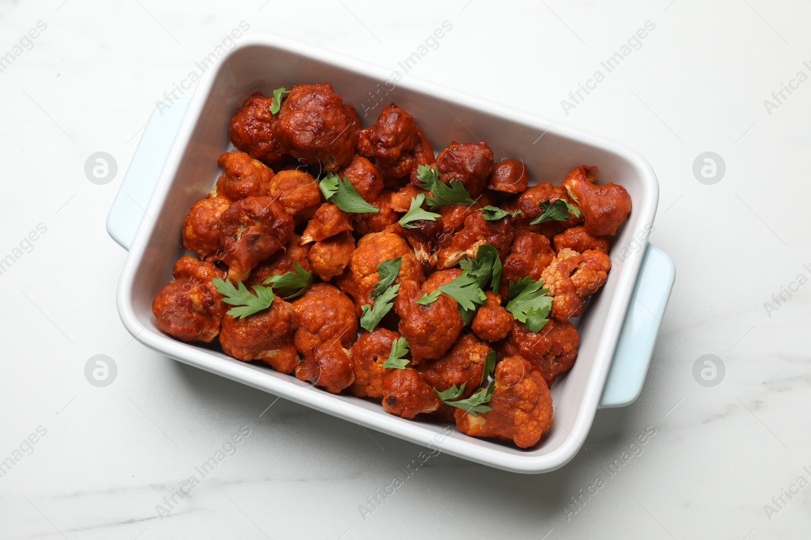 Photo of Baked cauliflower buffalo wings with parsley in baking dish on white marble table, top view