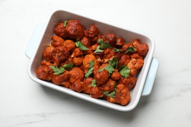 Photo of Baked cauliflower buffalo wings with parsley in baking dish on white marble table, top view