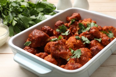 Photo of Baked cauliflower buffalo wings in baking dish and parsley on wooden table, closeup