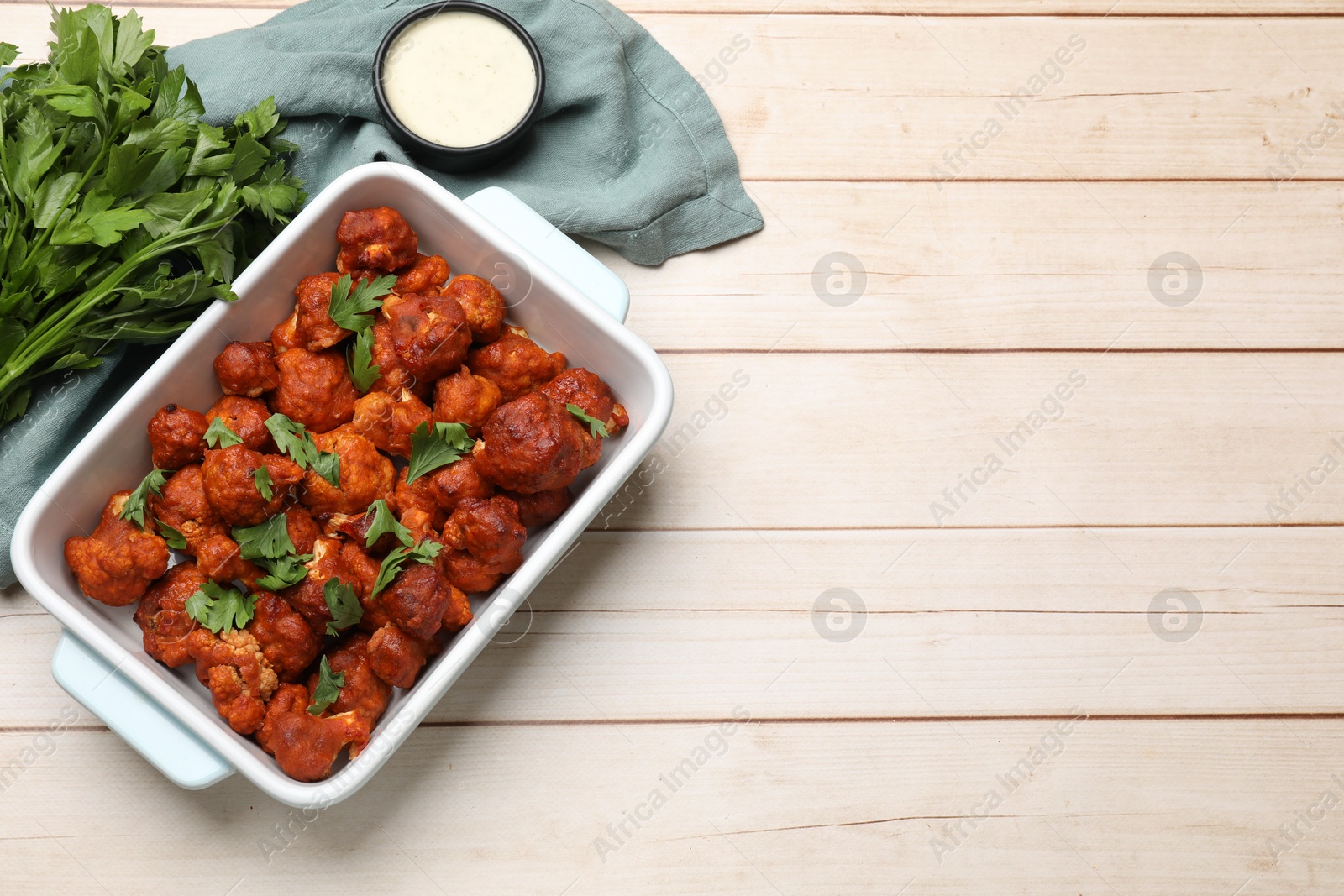 Photo of Baked cauliflower buffalo wings in baking dish, sauce and parsley on wooden table, top view. Space for text