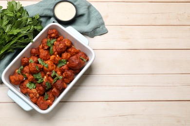 Photo of Baked cauliflower buffalo wings in baking dish, sauce and parsley on wooden table, top view. Space for text