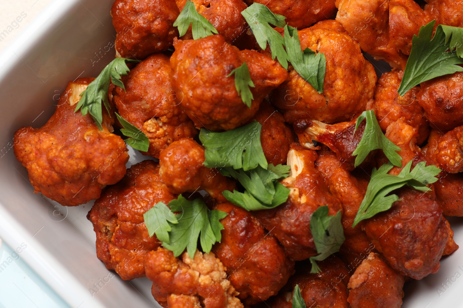 Photo of Baked cauliflower buffalo wings with parsley in baking dish, top view