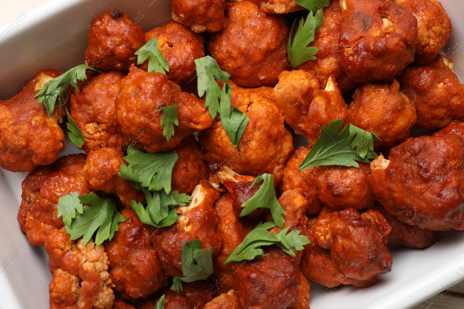 Photo of Baked cauliflower buffalo wings with parsley in baking dish, top view