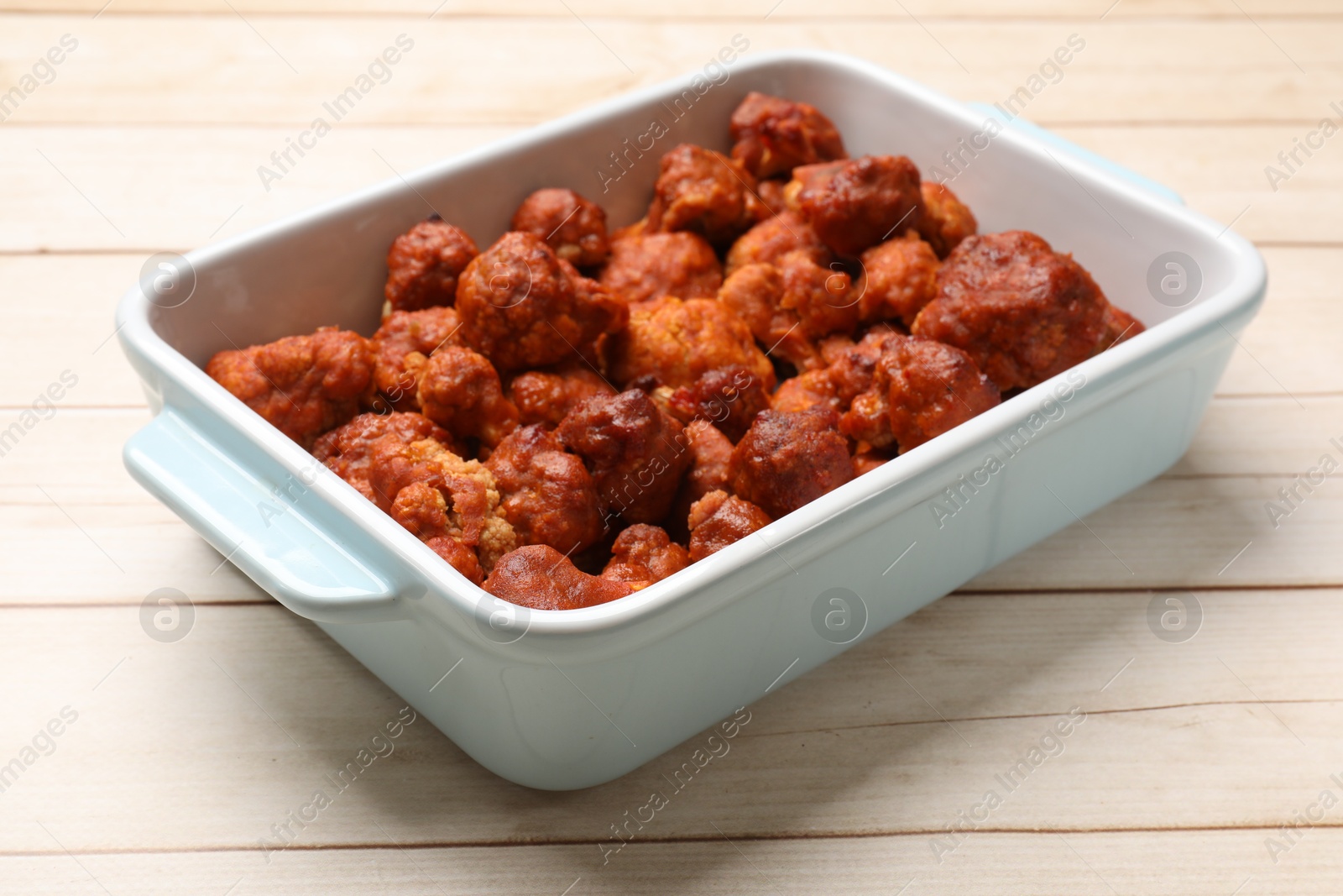 Photo of Baked cauliflower buffalo wings in baking dish on wooden table, closeup