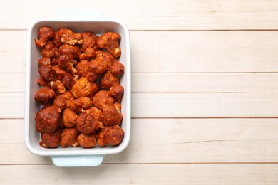 Photo of Baked cauliflower buffalo wings in baking dish on wooden table, top view. Space for text