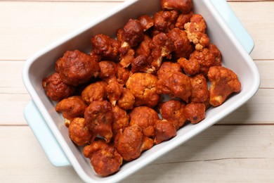 Photo of Baked cauliflower buffalo wings in baking dish on wooden table, top view