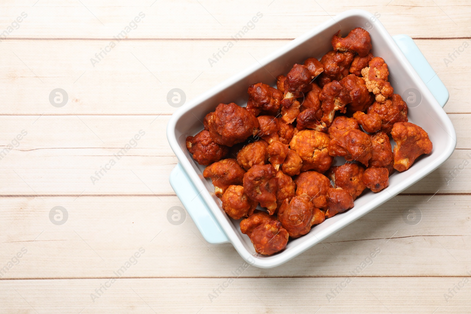 Photo of Baked cauliflower buffalo wings in baking dish on wooden table, top view. Space for text