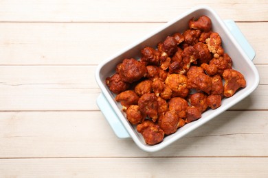 Photo of Baked cauliflower buffalo wings in baking dish on wooden table, top view. Space for text