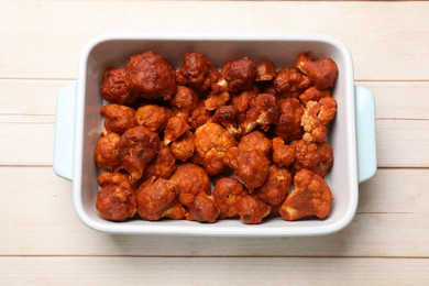 Photo of Baked cauliflower buffalo wings in baking dish on wooden table, top view