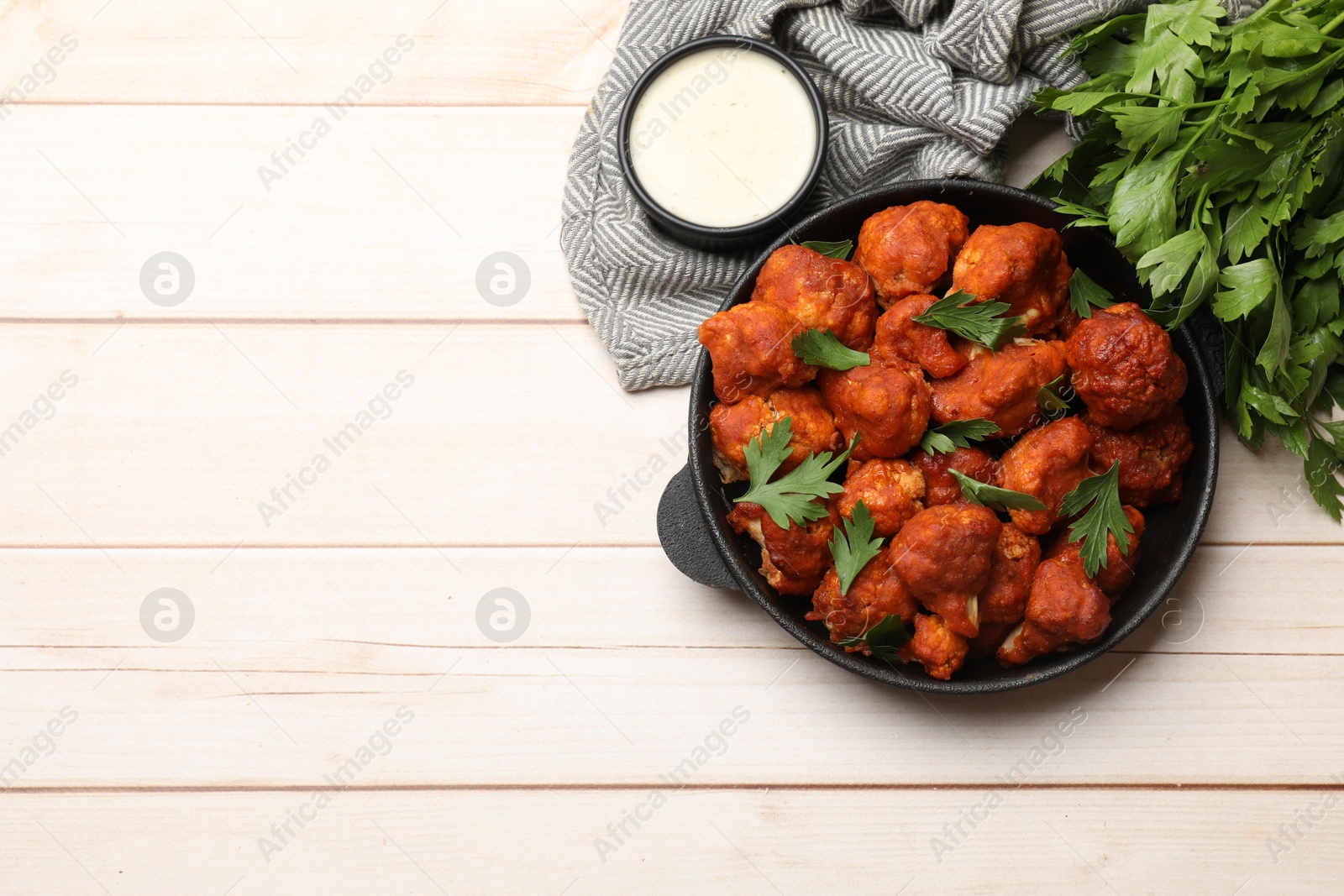 Photo of Baked cauliflower buffalo wings in baking dish, sauce and parsley on wooden table, top view. Space for text