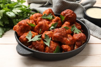 Photo of Baked cauliflower buffalo wings in baking dish and parsley on wooden table, closeup