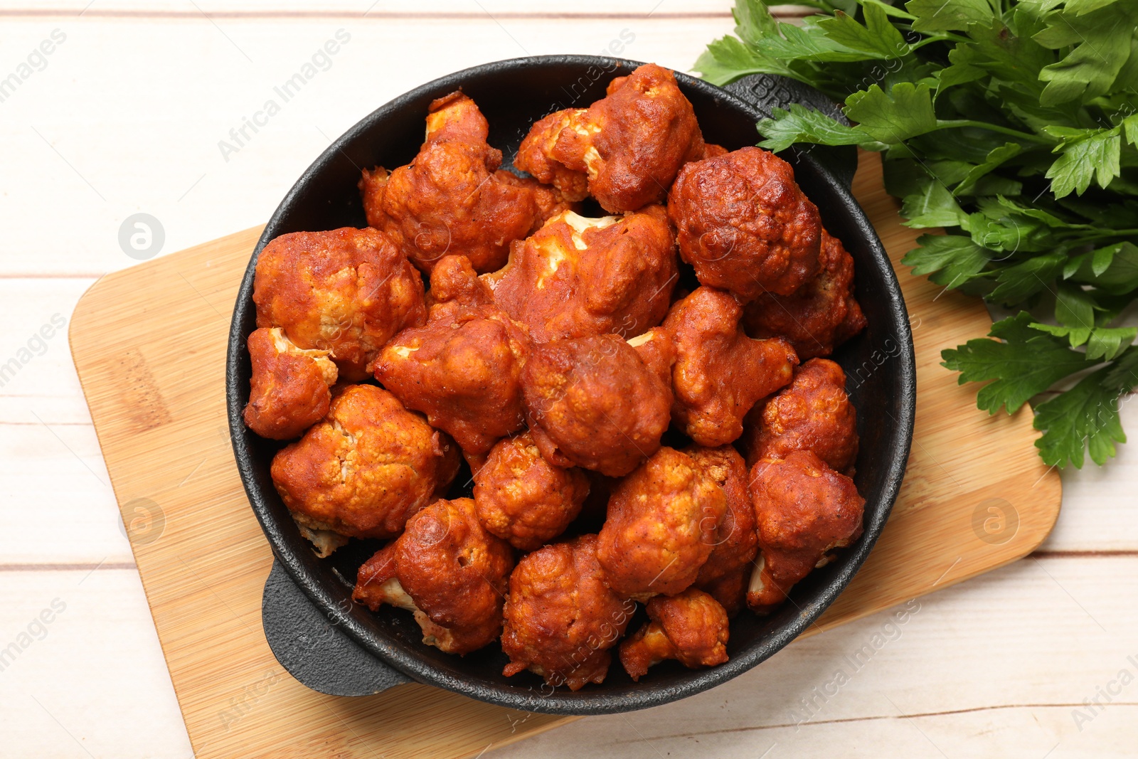 Photo of Baked cauliflower buffalo wings in baking dish and parsley on wooden table, top view