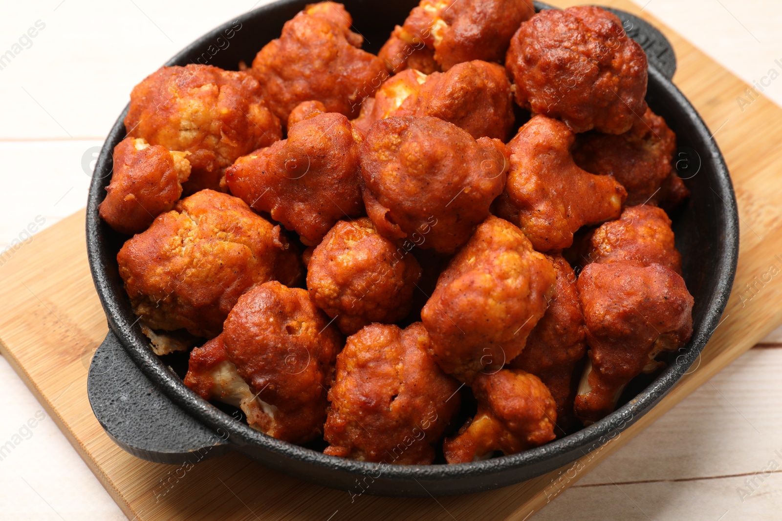 Photo of Baked cauliflower buffalo wings in baking dish on wooden table, closeup