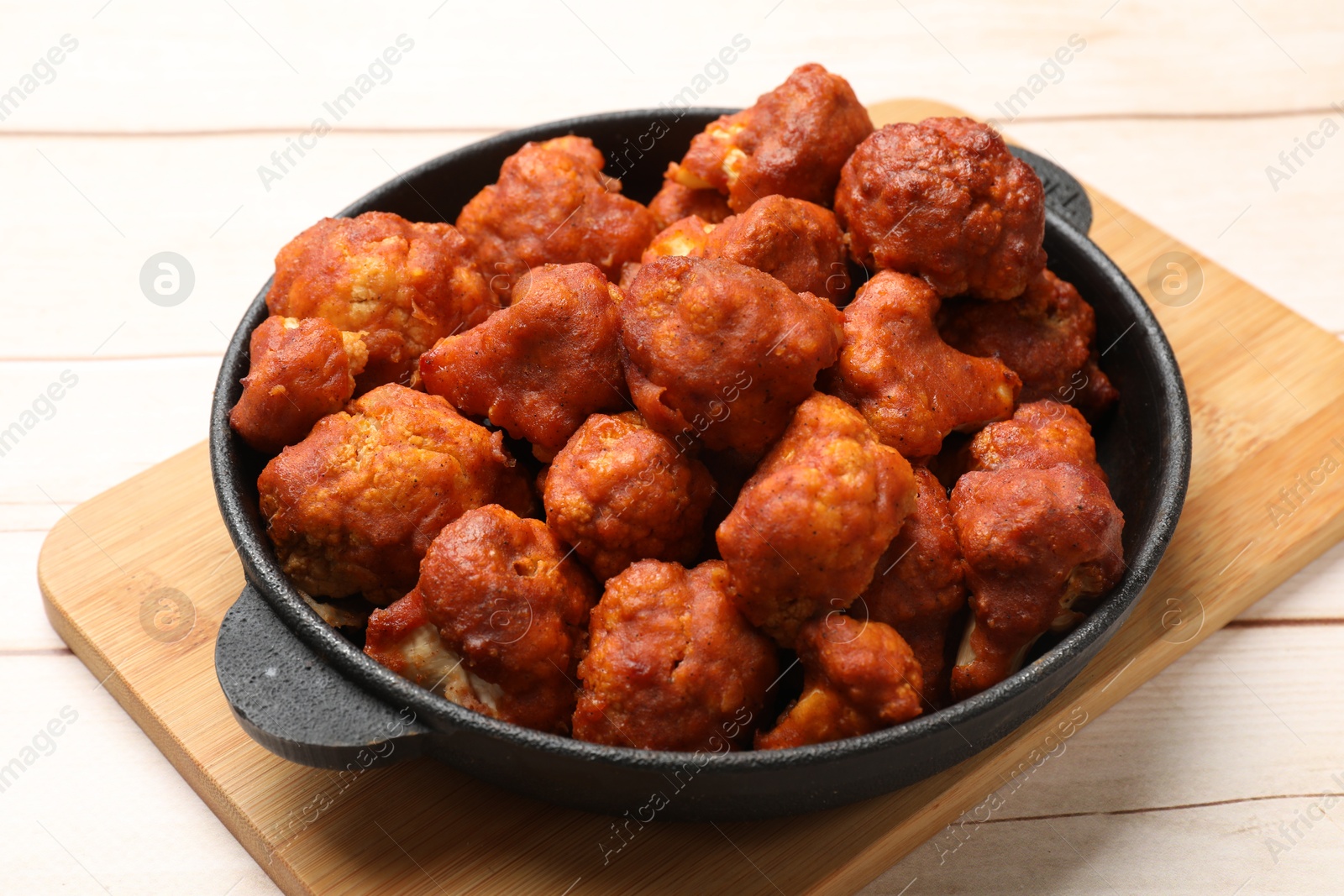 Photo of Baked cauliflower buffalo wings in baking dish on wooden table, closeup