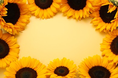 Frame made of sunflower heads on yellow background, flat lay. Space for text