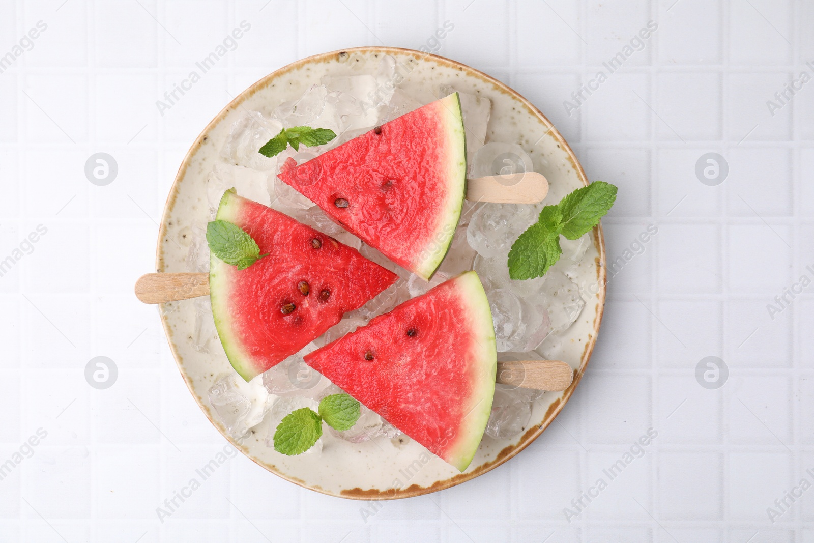 Photo of Pieces of tasty watermelon, ice cubes and mint on white tiled table, top view