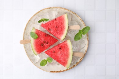 Photo of Pieces of tasty watermelon, ice cubes and mint on white tiled table, top view