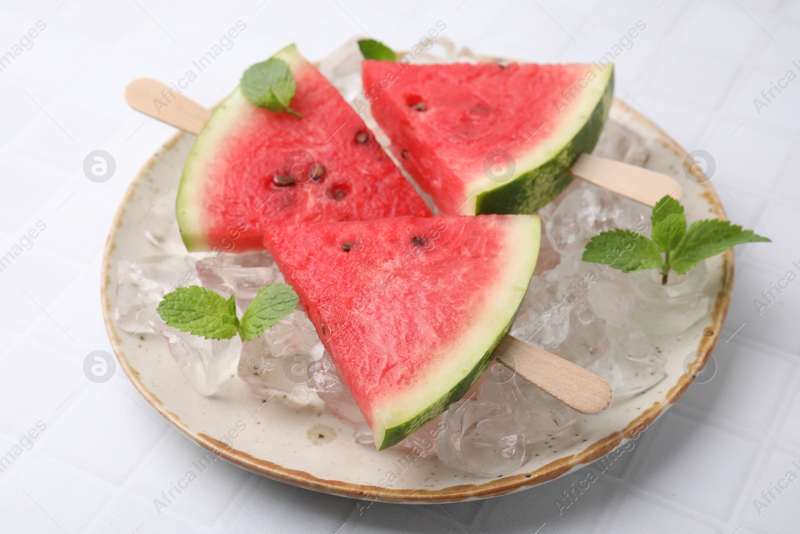 Photo of Pieces of tasty watermelon, ice cubes and mint on white tiled table, closeup