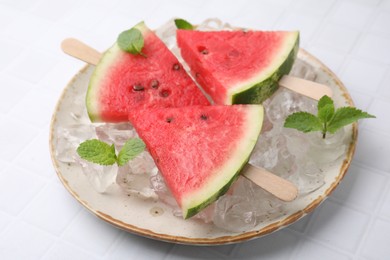 Photo of Pieces of tasty watermelon, ice cubes and mint on white tiled table, closeup