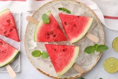 Photo of Pieces of tasty watermelon, ice cubes, lime and mint on white tiled table, flat lay