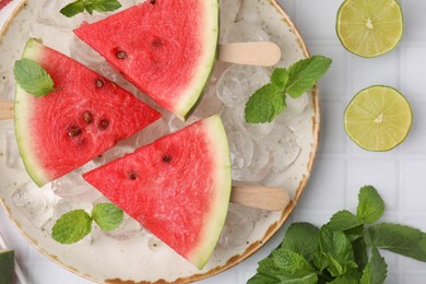 Photo of Pieces of tasty watermelon, ice cubes, lime and mint on white tiled table, flat lay