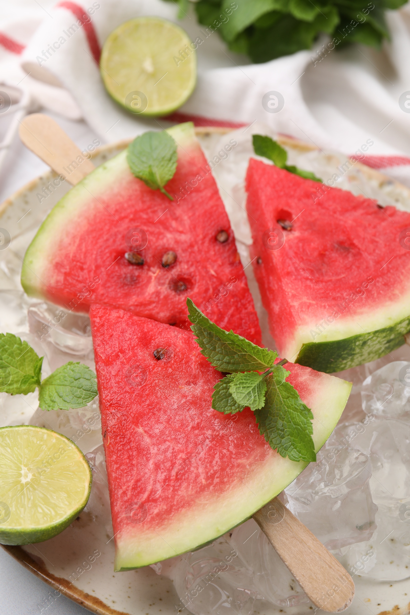 Photo of Pieces of tasty watermelon, ice cubes, lime and mint on table, closeup