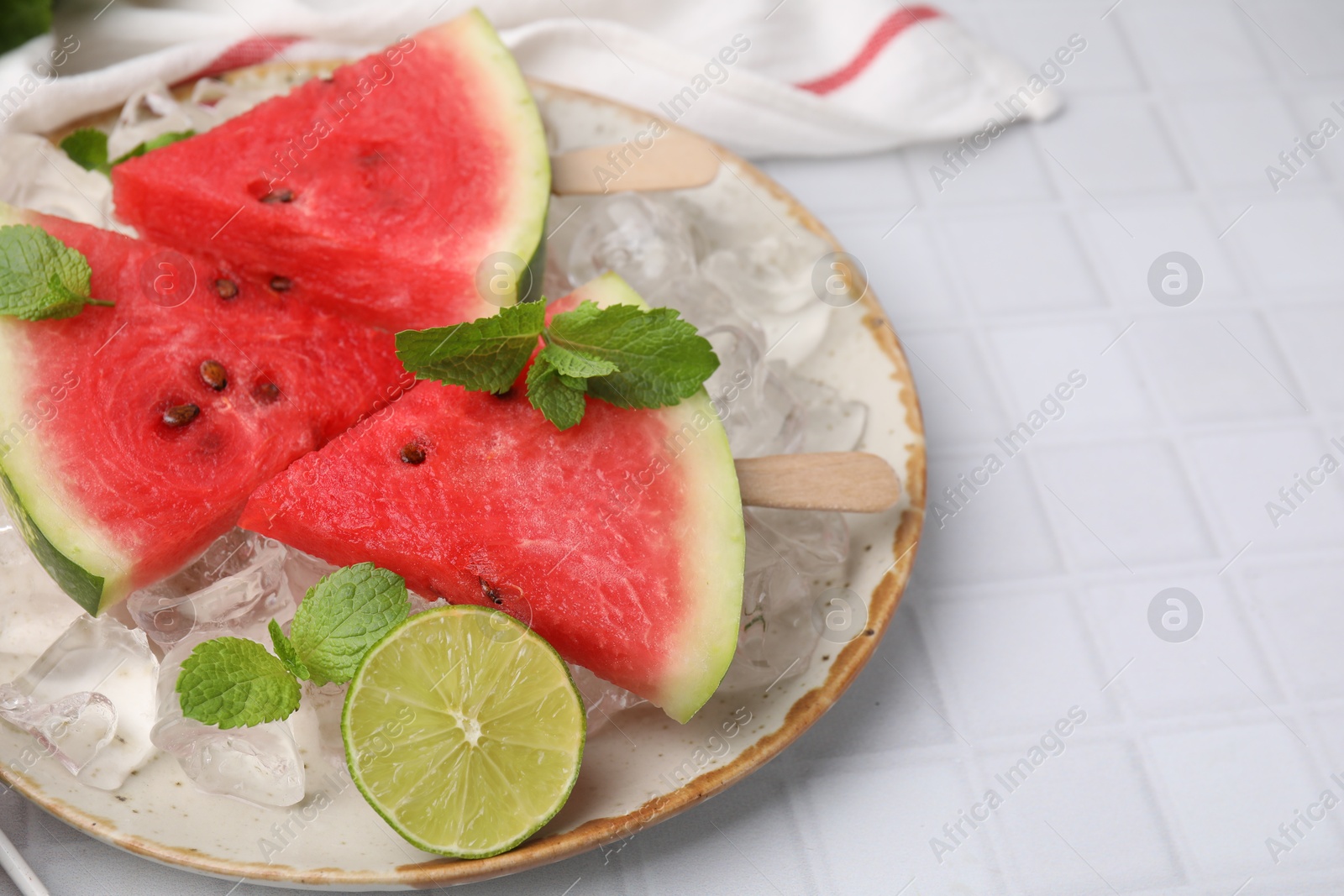 Photo of Pieces of tasty watermelon, ice cubes, lime and mint on white tiled table, closeup. Space for text