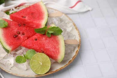 Photo of Pieces of tasty watermelon, ice cubes, lime and mint on white tiled table, closeup. Space for text