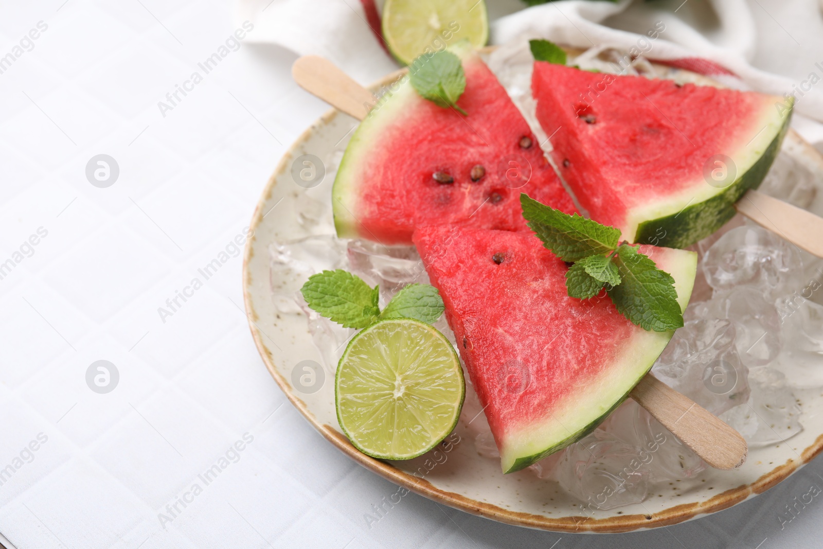 Photo of Pieces of tasty watermelon, ice cubes, lime and mint on white tiled table, closeup. Space for text