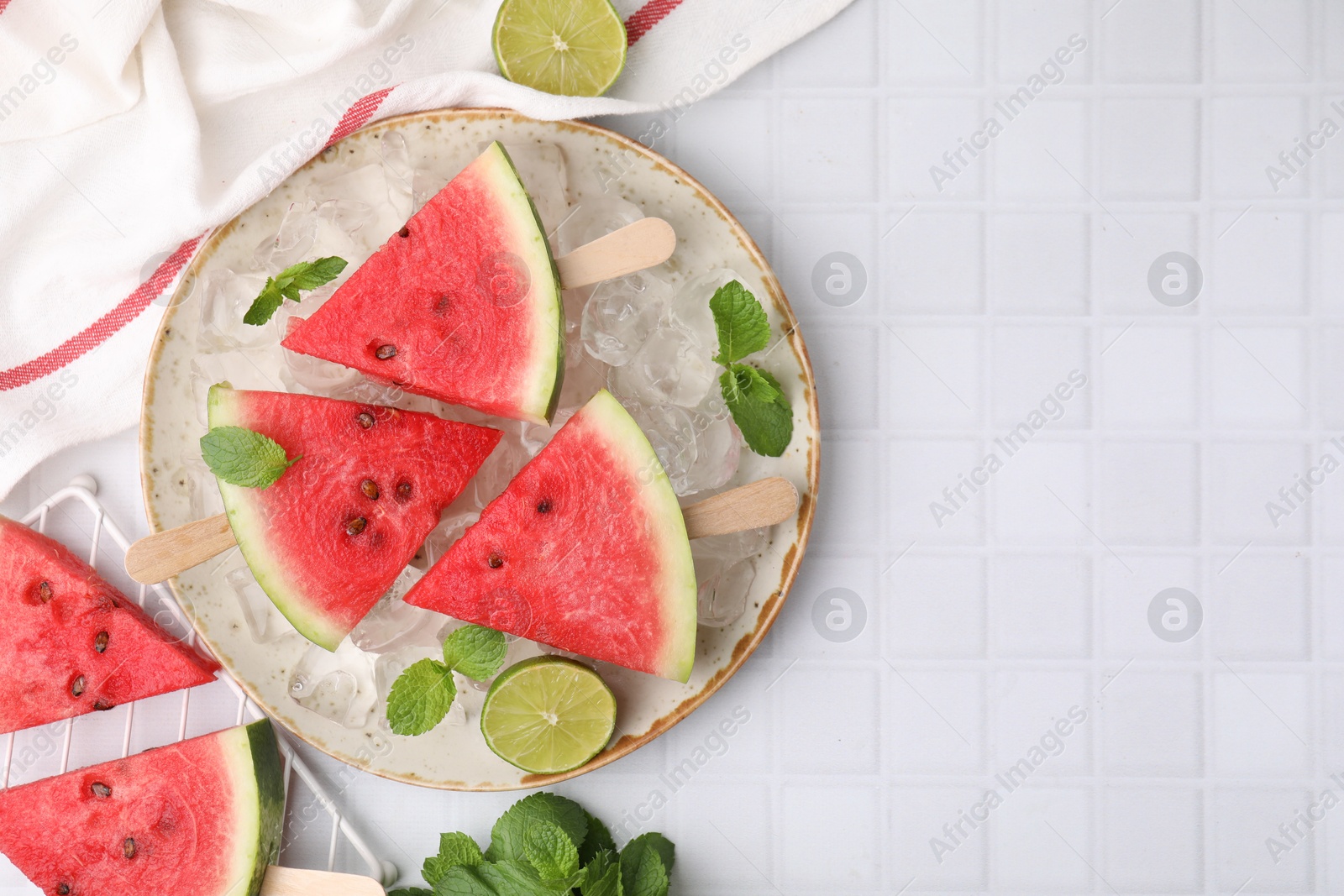 Photo of Pieces of tasty watermelon, ice cubes, lime and mint on white tiled table, flat lay. Space for text