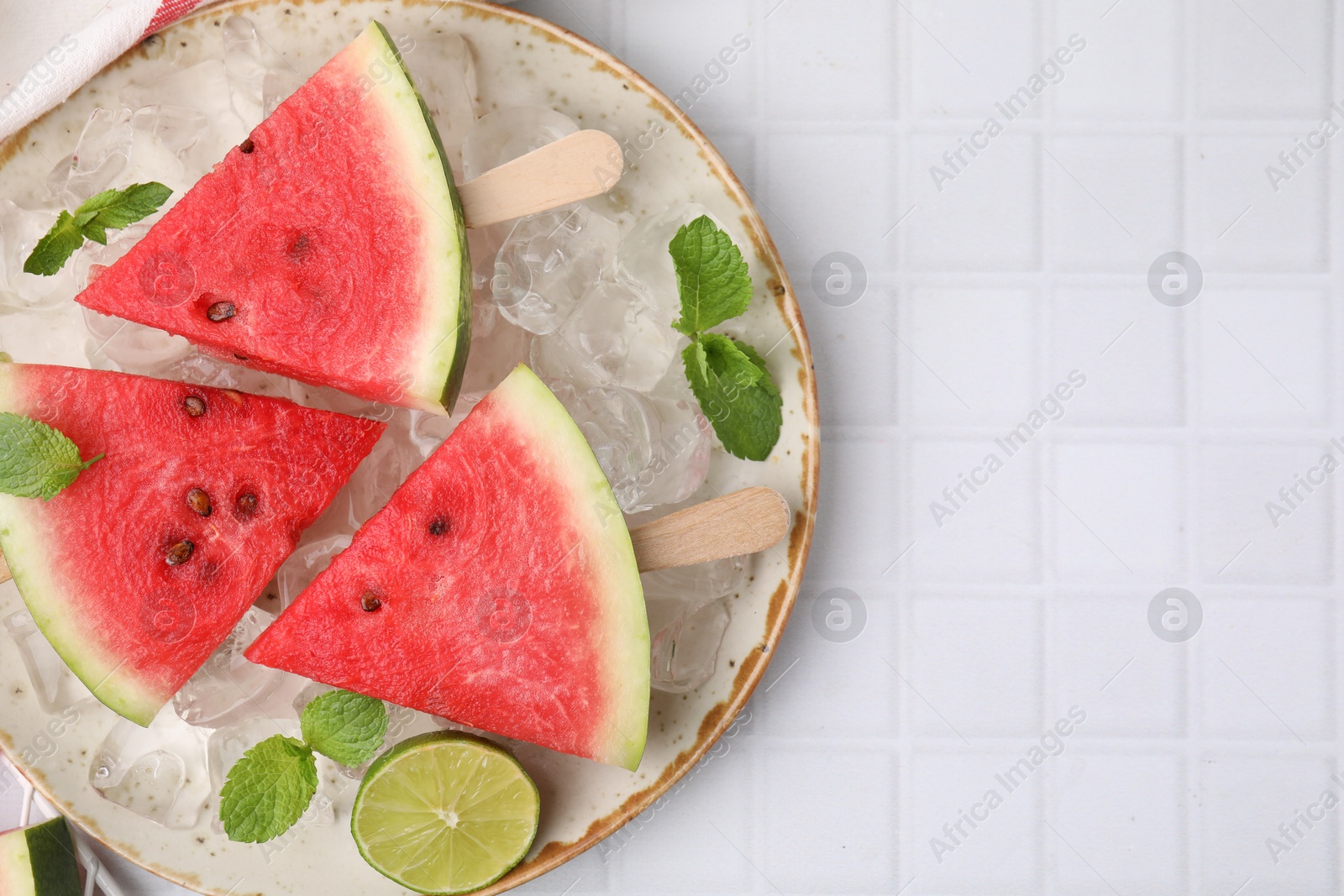 Photo of Pieces of tasty watermelon, ice cubes, lime and mint on white tiled table, top view. Space for text