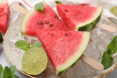 Photo of Pieces of tasty watermelon, ice cubes, lime and mint on table, closeup