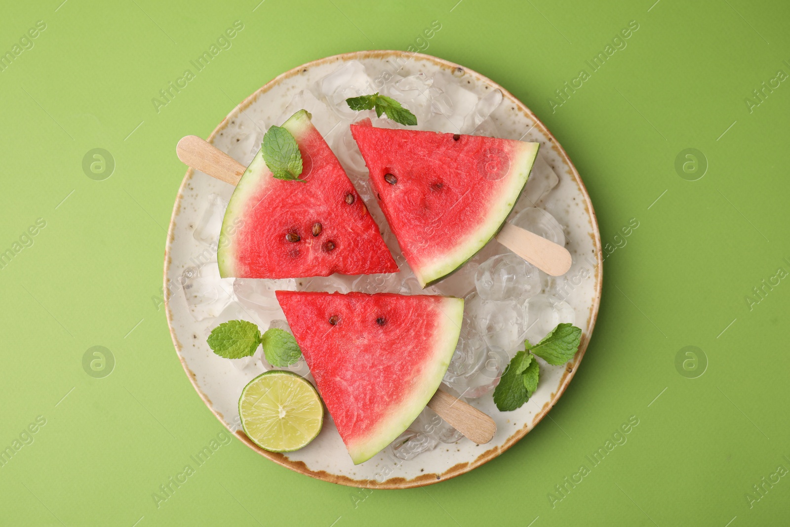 Photo of Pieces of tasty watermelon, ice cubes, lime and mint on green table, top view