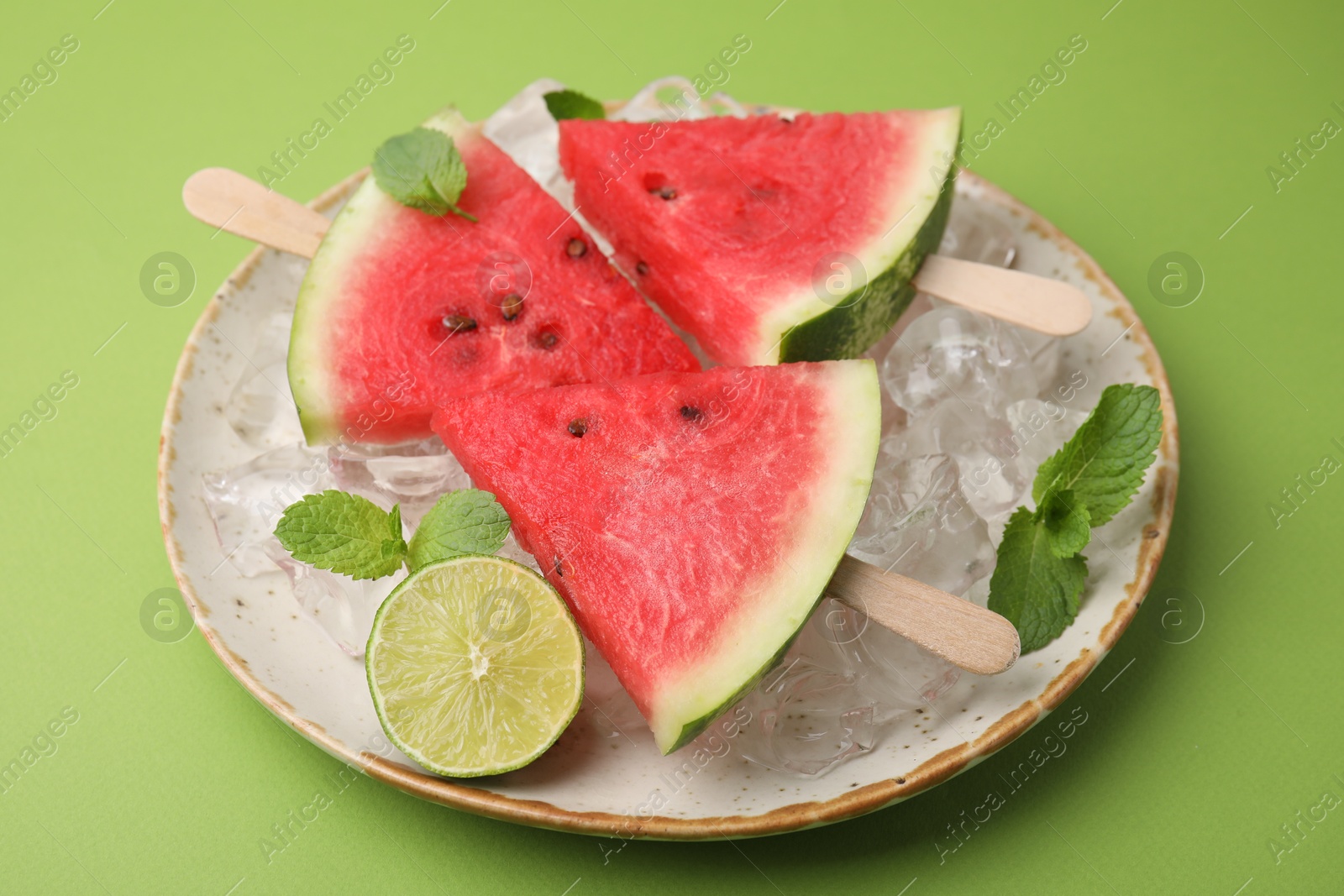 Photo of Pieces of tasty watermelon, ice cubes, lime and mint on green table, closeup