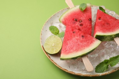 Photo of Pieces of tasty watermelon, ice cubes, lime and mint on green table, closeup. Space for text