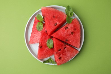 Photo of Pieces of tasty watermelon and mint on green table, top view