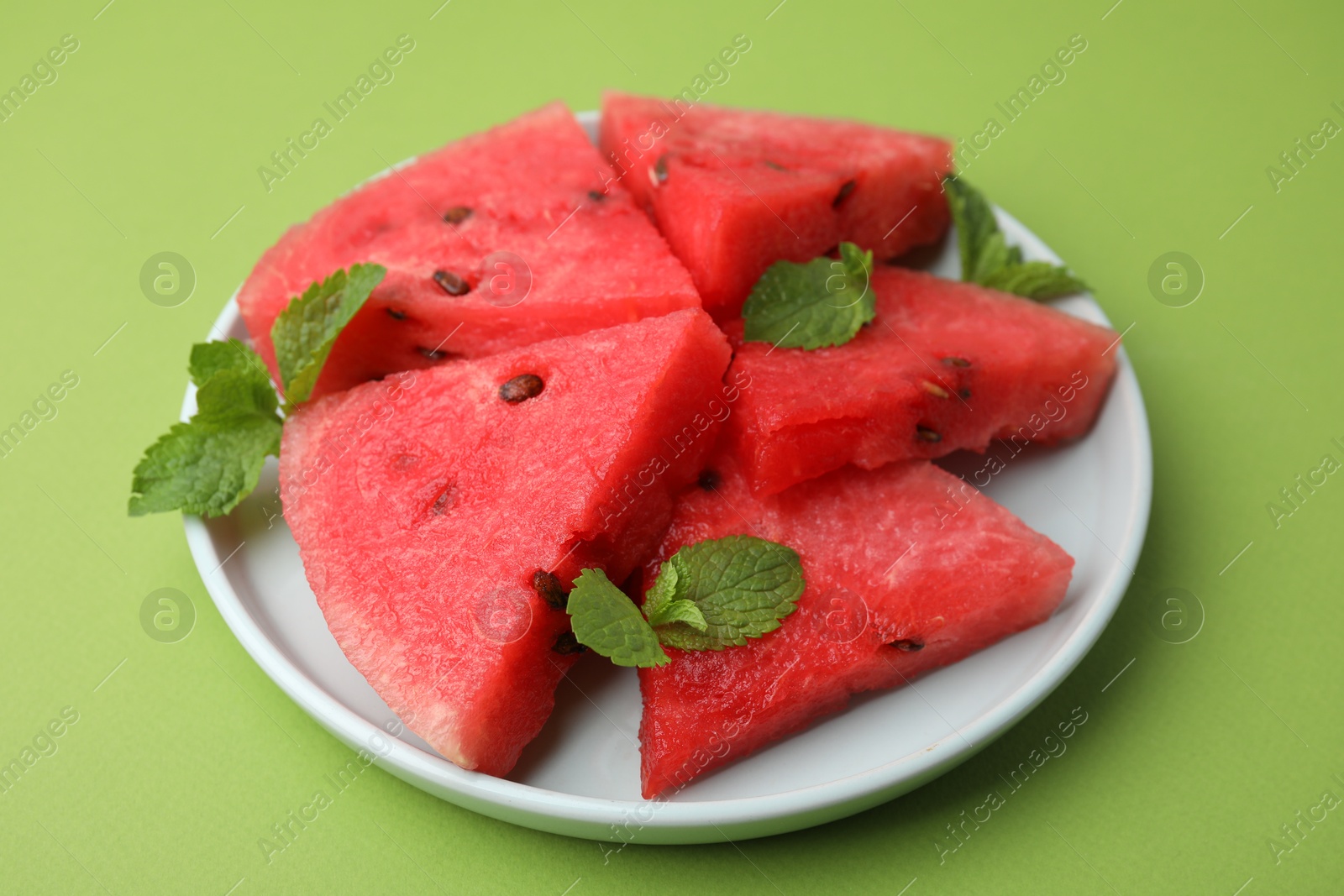 Photo of Pieces of tasty watermelon and mint on green table, closeup