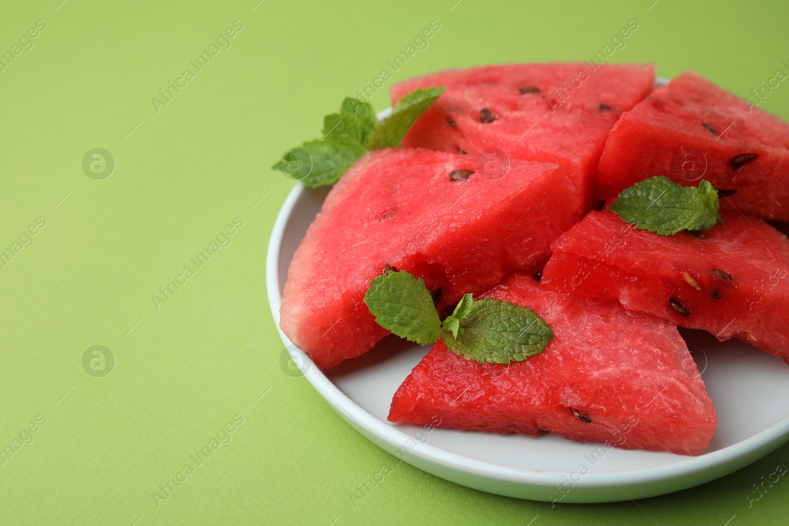 Photo of Pieces of tasty watermelon and mint on green table, closeup. Space for text