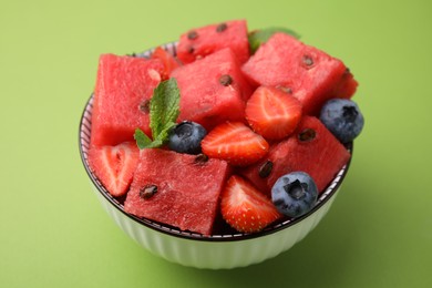 Photo of Pieces of tasty watermelon, strawberries, blueberries and mint in bowl on green table, closeup