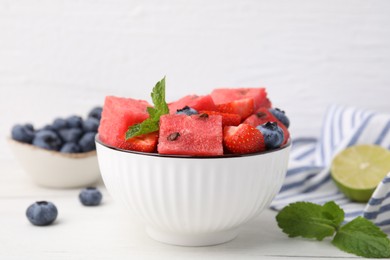 Photo of Pieces of tasty watermelon, strawberries, blueberries and mint in bowl on white wooden table, closeup