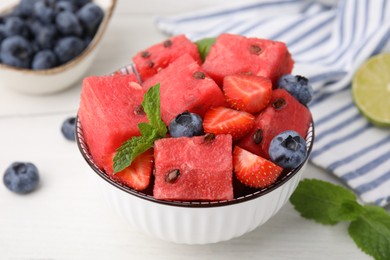 Photo of Pieces of tasty watermelon, strawberries, blueberries and mint in bowl on white wooden table, closeup