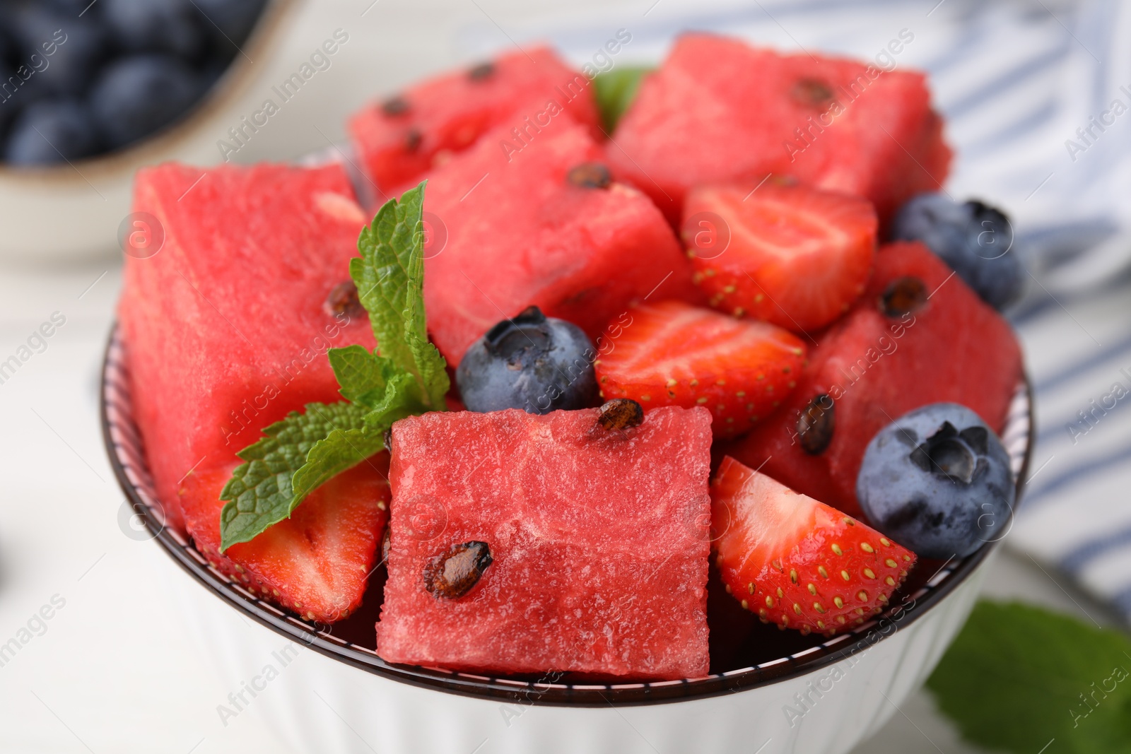 Photo of Pieces of tasty watermelon, strawberries, blueberries and mint in bowl on table, closeup