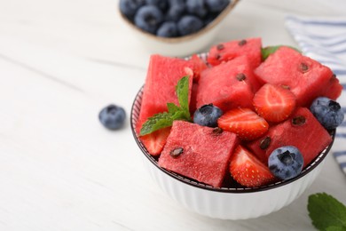 Pieces of tasty watermelon, strawberries, blueberries and mint in bowl on white wooden table, closeup. Space for text