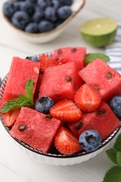 Photo of Pieces of tasty watermelon, strawberries, blueberries and mint in bowl on white wooden table, closeup