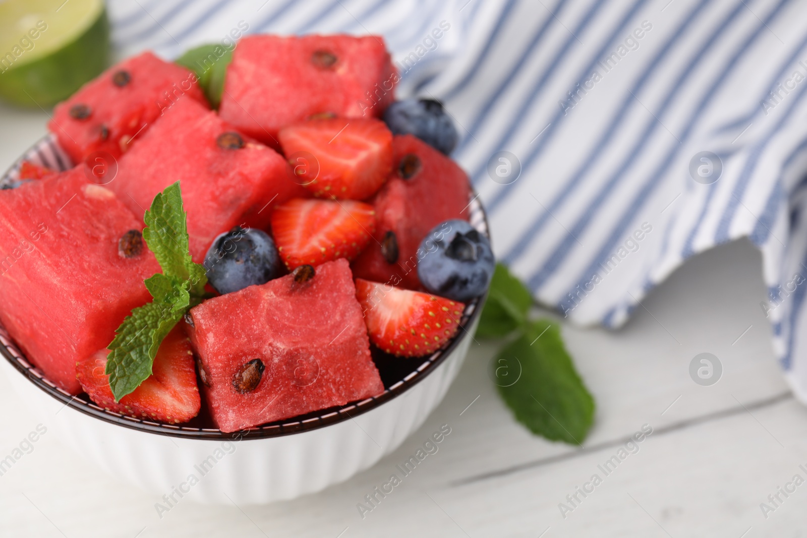 Photo of Pieces of tasty watermelon, strawberries, blueberries and mint in bowl on white wooden table, closeup