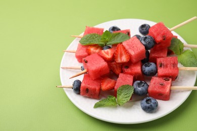 Photo of Skewers with tasty watermelon, strawberries, blueberries and mint on green table, closeup