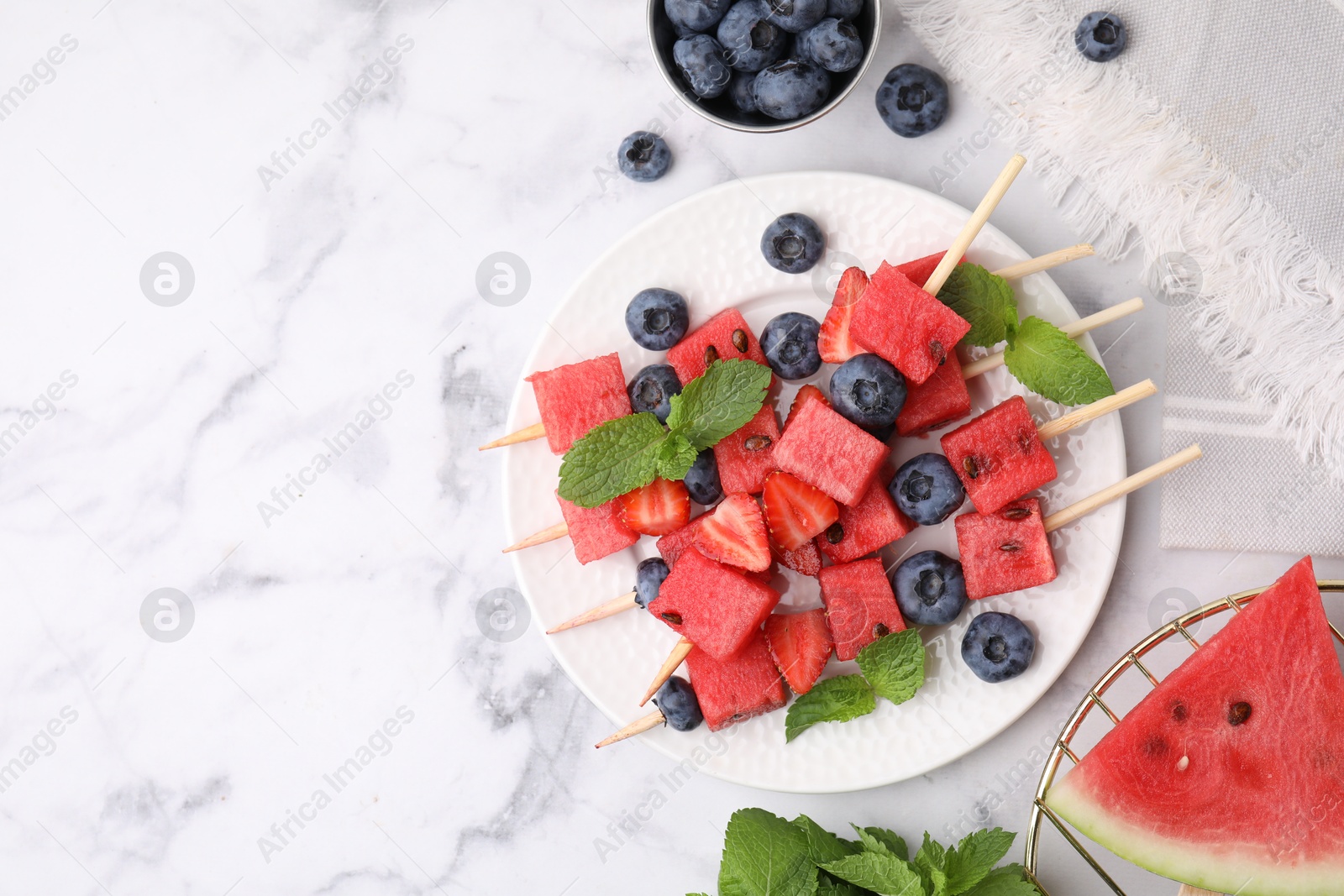 Photo of Skewers with tasty watermelon, strawberries, blueberries and mint on white marble table, flat lay. Space for text