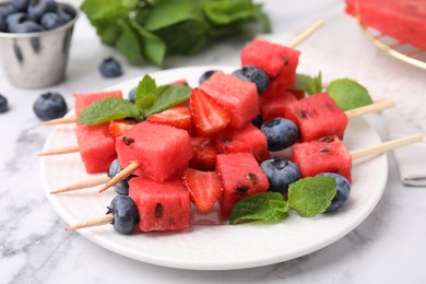 Photo of Skewers with tasty watermelon, strawberries, blueberries and mint on white marble table, closeup